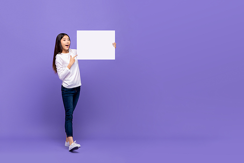 Smiling cheerful Asian woman pointing hand to blank paper isolated on purple background with copy space