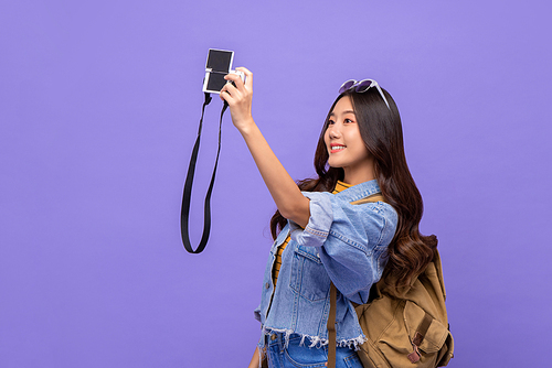 Smiling young Asian woman tourist backpacker taking selfie with camera isolated on purple background