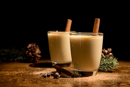 Homemade traditional Christmas eggnog drinks with ground nutmeg, cinnamon and decorating items on wood table, preparing for celebrating festive holiday season