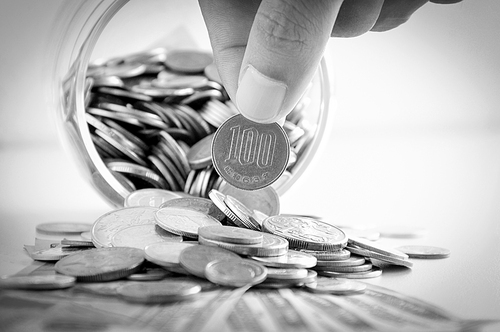 Hand picking up 100 Japanese yen (JPY) coin out of multi currency pile of coins - monochrome effect