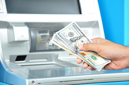 Hand holding money United States dollar (USD) bills in front of ATM