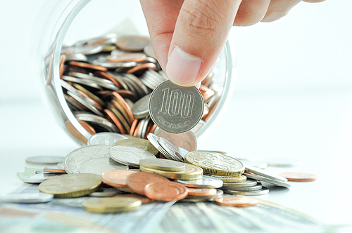 Hand picking up 100 Japanese yen (JPY) coin out of multi-currency pile of coins