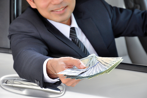 Businessman sitting inside the car giving money - car rental & leasing concept