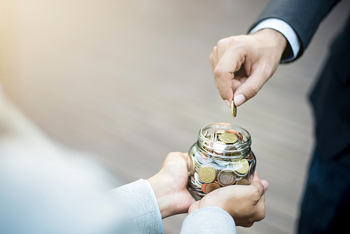 Businessman hand putting money (coin) in the glass jar held by a woman