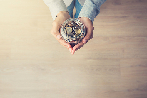 Young woman hands holding glass jar with coins inside - top view, vintage tone, with copy space