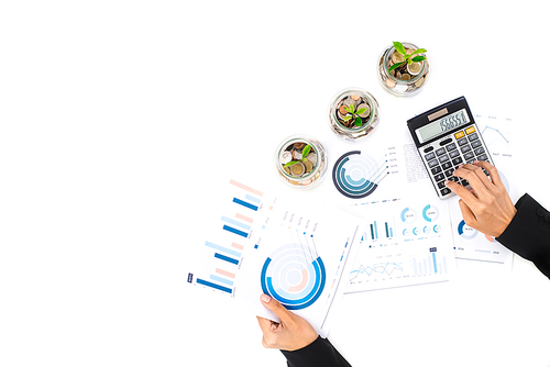 Woman working at worktable with some plants growing from coin (money) in the glass jars, financial background concept, top view