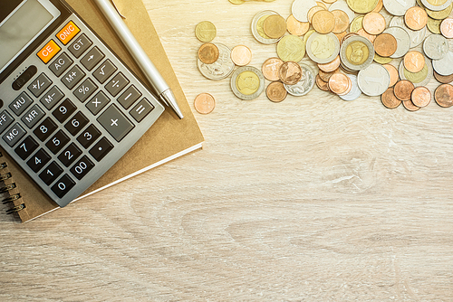 Money (coins), calculator and some stationery on wood table, top view with copy space - financial background concept