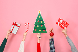 Hands holding gift boxes and colorful Christmas decorating items on pink isolated background