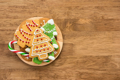 Colorful decorated Christmas gingerbread cookies and candy cane on wood background, top view  with copy space
