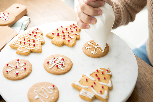 Young woman decorating homemade gingerbread Christmas cookies with royal icing sugar on white platter