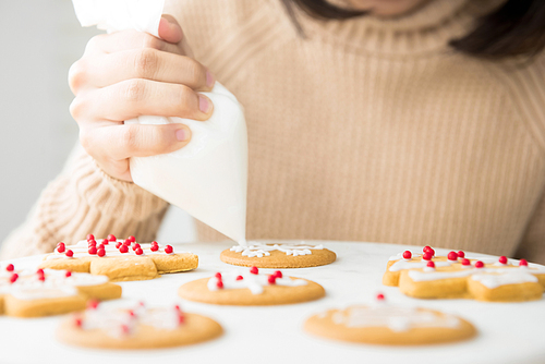 Young woman decorating homemade gingerbread Christmas cookies with royal icing sugar on white platter at bakery