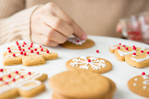 Homemade Christmas gingerbread cookies being decorated by a woman on white platter