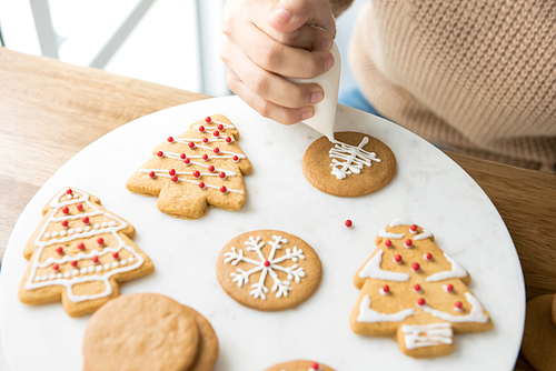 Young woman decorating homemade gingerbread Christmas cookies with royal icing sugar on white platter