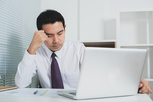 Asian businessman getting stressed at work in front of laptop computer - soft tone