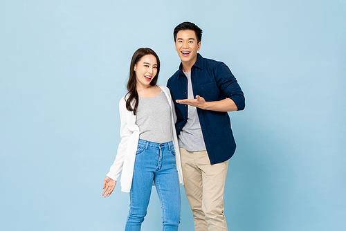 Surprised smiling Asian couple in casual clothes standing in light blue isolated studio background