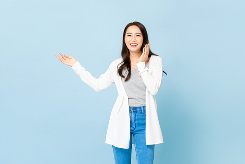 Smiling young pretty Asian woman with hands opening sideways in isolated light blue background