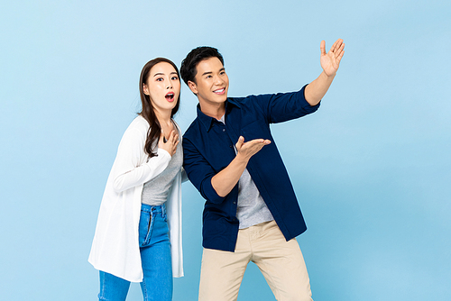 Shocked amazed Asian couple pointing hands up to empty space above on isolated light blue background
