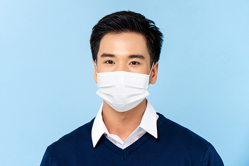 Close up portrait of young handsome Asian man wearing medical face mask isolated on light blue background