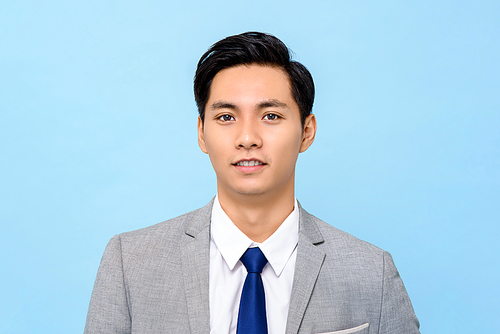 Portrait of  young handsome Asian man in formal business suit isolated on light blue background
