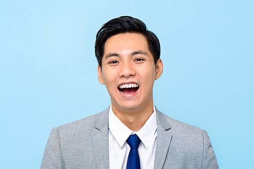 Close up portrait of happy young Asian businessman laughing isolated studio blue background
