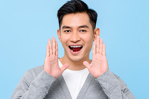 Close up portrait of smiling attractive Asian man looking surprised with opened mouth and open palms  in isolated studio blue background
