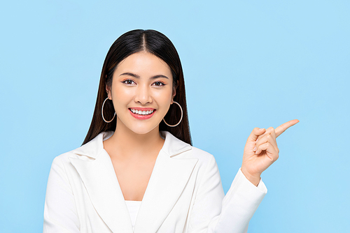 Pretty Asian woman in white suit smiling and pointing finger to space aside isolated on light blue background