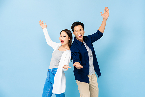 Surprised Asian couple standing back to back smiling and opening hands in light blue isolated studio background