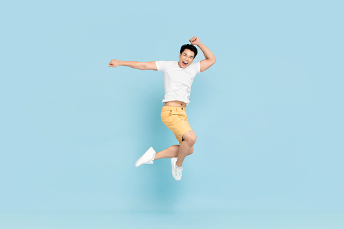 Happy handsome Asian young man in casual clothes smiling and jumping in light blue pastel background