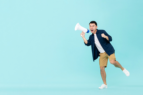 Excited young Asian man holding megaphone and shouting isolated on light blue background with copy space