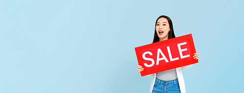 Surprised Asian woman holding sale sign isolated on blue banner background with copy space