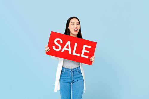 Surprised Asian woman holding red sale sign isolated on light blue background