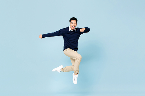 Young handsome Asian man smiling and jumping in mid-air on light blue studio background