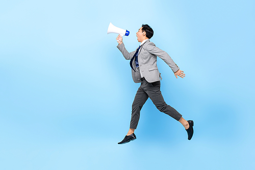 Young Asian businessman jumping and shouting on megaphone isolated on light blue background