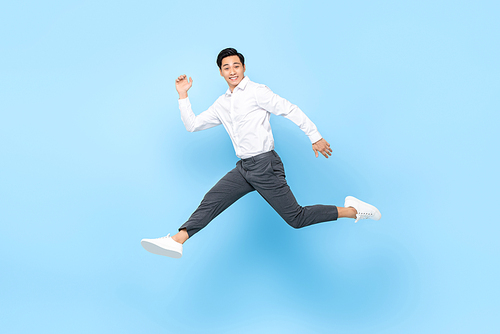 Happy smiling energetic Asian man in semi formal clothes jumping in mid air isolated on light blue background