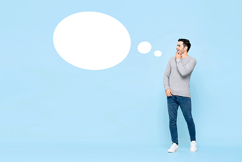 Cheerful young handsome caucasian man thinking and looking at empty white speech bubble isolated on light blue background