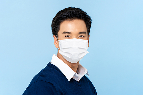 Close up portrait of young handsome Asian man wearing medical face mask isolated on light blue background