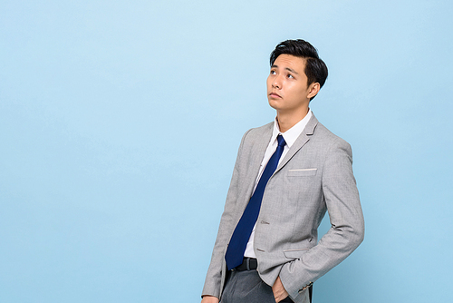Bored Asian businessman thinking and looking up to copy space aside in isolated light blues studio background