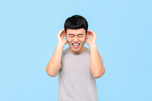 Funny portrait of laughing young Asian man holding his ears with both hands in isolated studio blue background