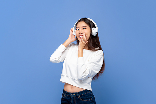 Young pretty Asian woman wearing wireless headphones listening to music isolated on light blue background