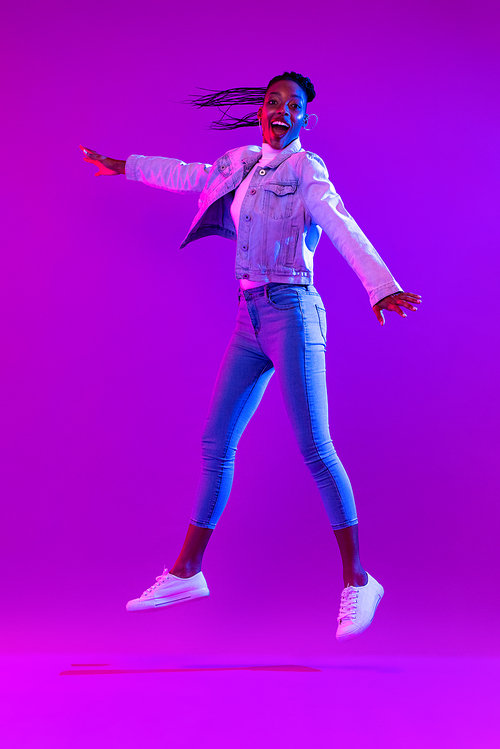 Trendy stylish energetic young African American woman jumping in futuristic purple cyberpunk neon light background