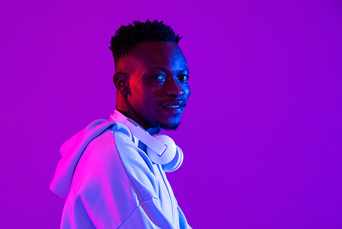 Young handsome African man with headphones in purple futuristic neon light studio background