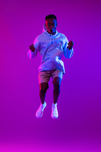 Young ecstatic African man jumping in futuristic purple cyberpunk neon light background