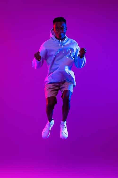 Young ecstatic African man jumping in futuristic purple cyberpunk neon light background