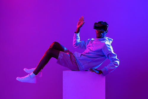Young African man wearing VR glass headset in futuristic purple cyberpunk neon light background
