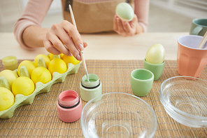 Closeup of unrecognizable young woman painting eggs in pastel colors for Easter while sitting at table in kitchen or art studio, copy space