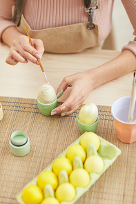 Top view close up of young woman painting eggs in pastel colors for Easter while sitting at table in kitchen or art studio, copy space