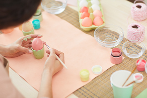 High angle close up of unrecognizable woman painting Easter eggs in pastel colors while sitting at table in kitchen or art studio, copy space
