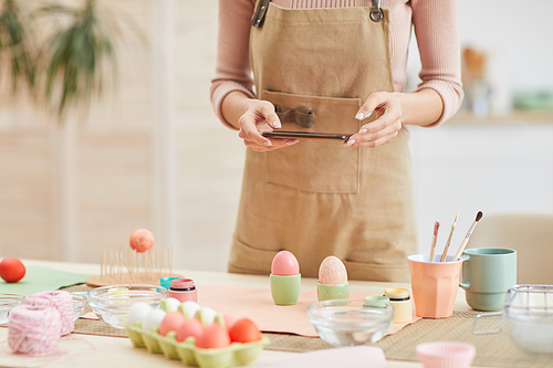 Cropped portrait of unrecognizable young woman taking smartphone photo of Easter eggs composition in art studio, copy space