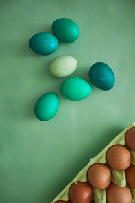 Above view of painted Easter eggs next to egg crate arranged in minimal composition on green background, copy space