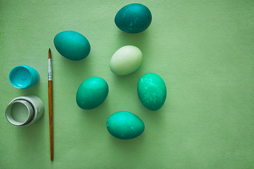 Above view of emerald Easter eggs arranged in minimal composition with paint brush on green background, copy space